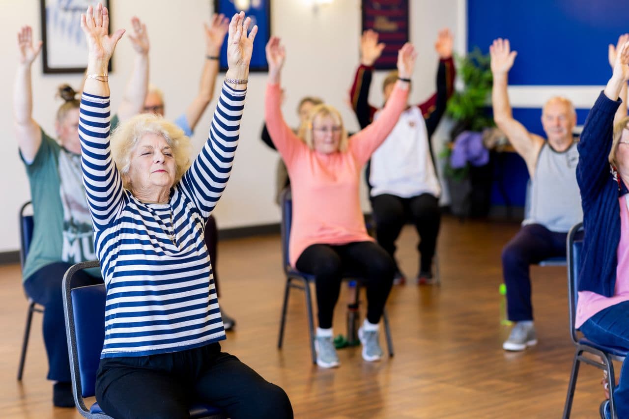 Older adults taking part in a seated group exercise class with their arms raised