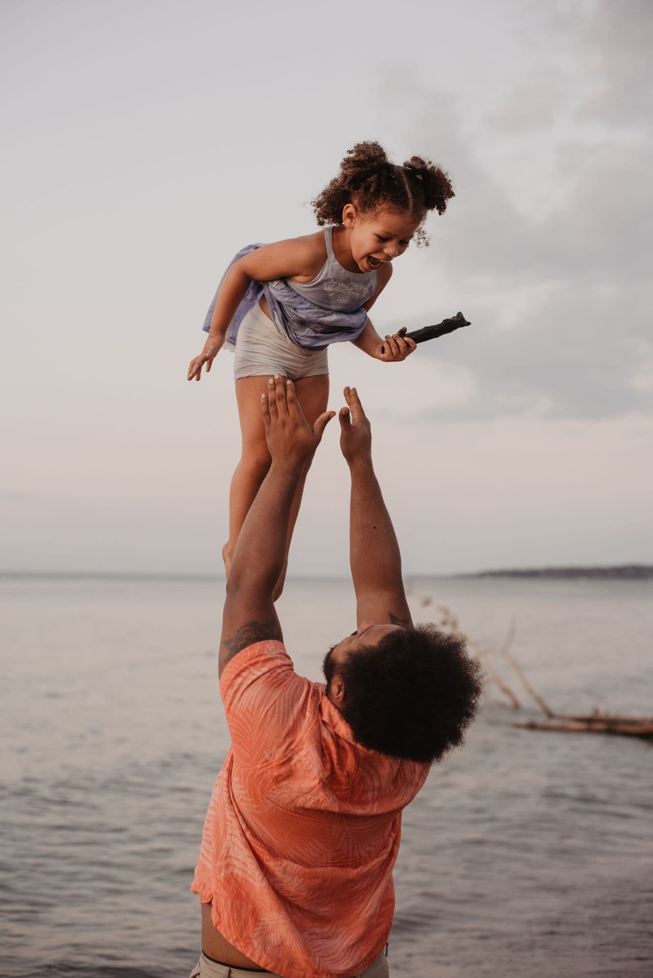 A parent lifting a laughing child by the water, sharing a moment of family connection